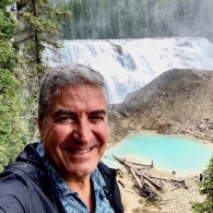 A photo of Miguel A. Romero in front of a waterfall. 